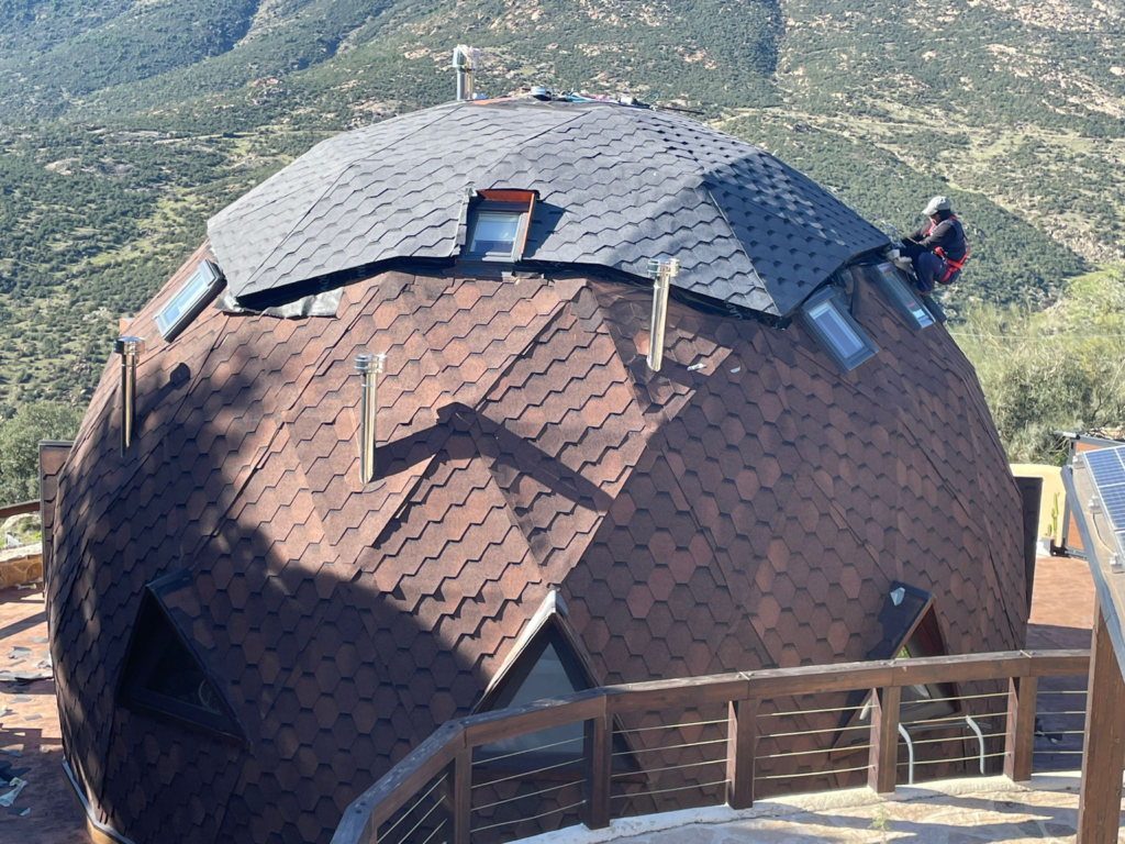 Domo geodésico con cubierta de tégola asfálticas durante trabajo de instalación en entorno natural.