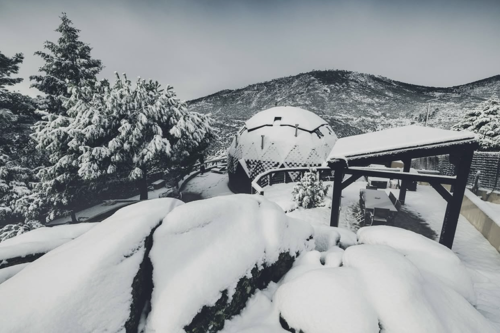 Domo geodésico cubierto de nieve, integrado en el paisaje, con alto aislamiento y diseño sostenible.