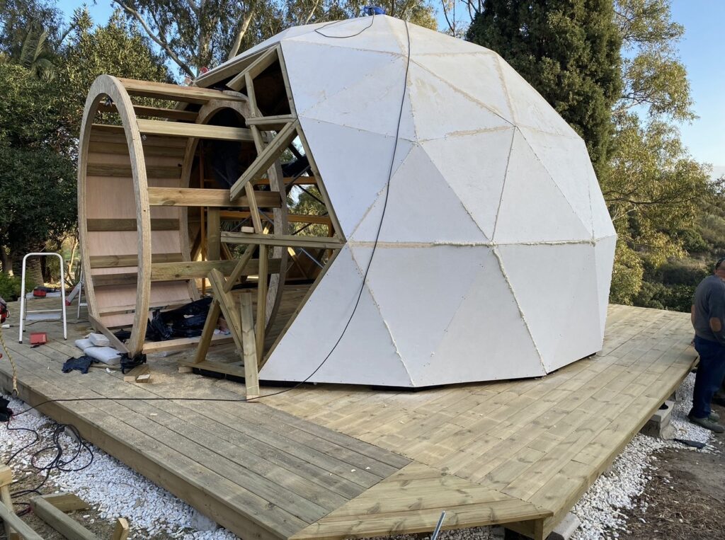 Montaje de envolvente en domo geodésico con paneles triangulares exteriores y estructura portante de madera sobre plataforma.